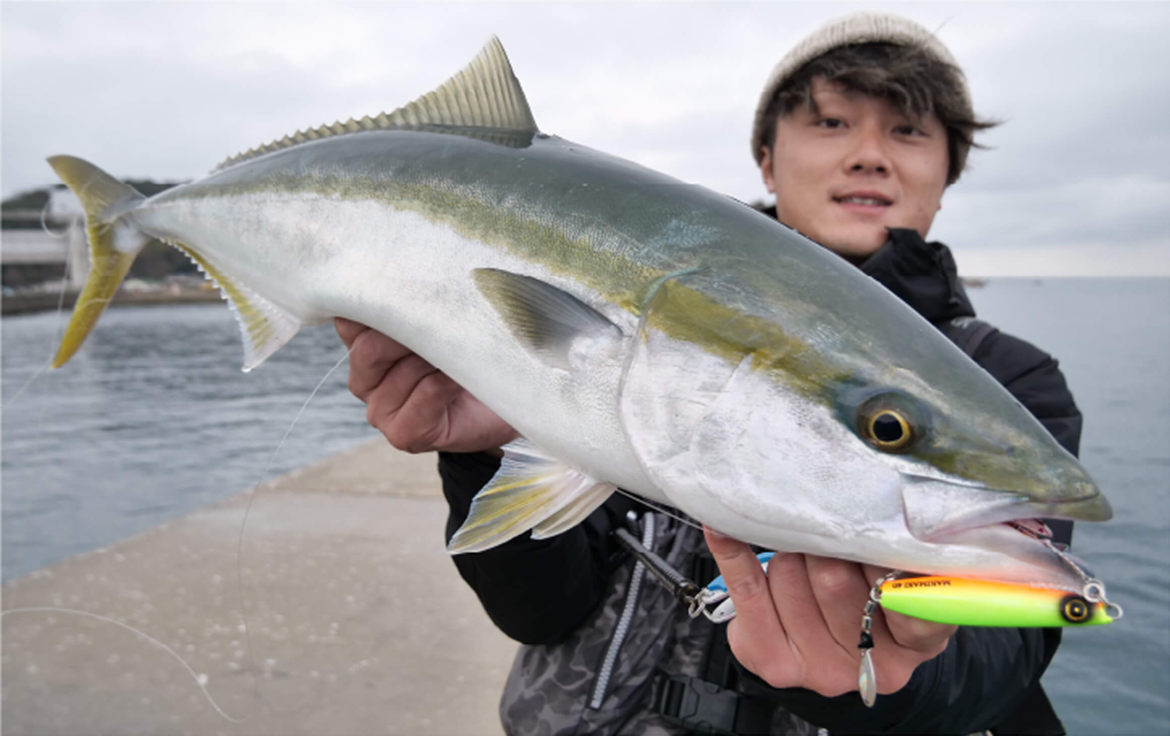海辺でマキマキ NEW COLORを使用して釣った魚を抱えている男性の写真